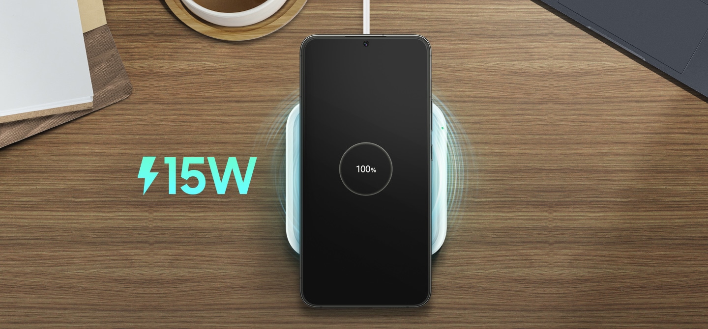 Một bộ sạc không dây 15W duy nhất có nguồn điện được kết nối trên một chiếc bàn gỗ. Một chiếc Galaxy S22 + màu đen với dòng chữ 100% "trên màn hình nằm trên bộ sạc.
